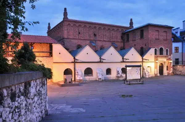 Stara synagoga w Krakowie o zmierzchu. Ceglana fasada, jasne przybudówki i kamienny dziedziniec tworzą historyczny klimat.