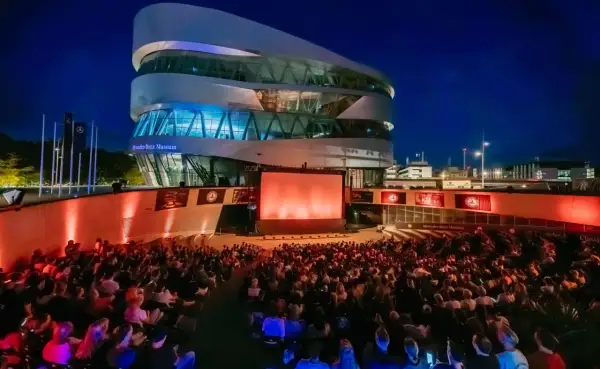 Ein großes Publikum genießt einen Filmabend beim Mercedes-Benz Museum Open Air. Die moderne Architektur des Museums bildet die beeindruckende Kulisse.