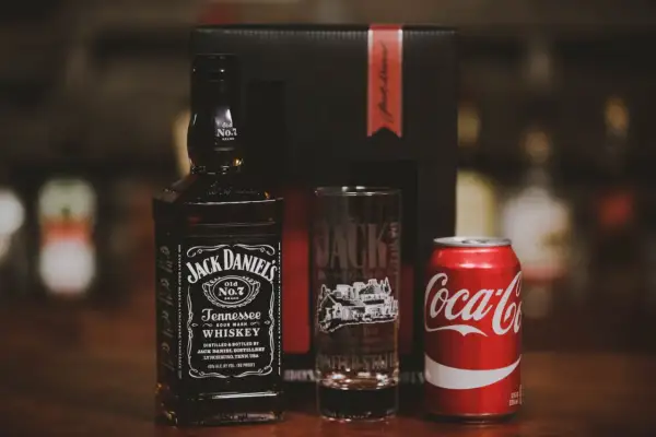 Zestaw na drinka: butelka Jack Daniel's, szklanka z logo destylarni i puszka Coca-Coli. Idealny na wieczór z klasycznym jack and coke.
