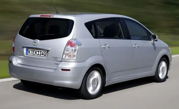 Srebrny Toyota Corolla Verso 2005 jedzie po drodze, w tle zielone wzgórza.