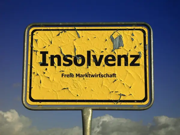 Gelbes, verwittertes Ortsschild mit der Aufschrift "Insolvenz" und "Freie Marktwirtschaft". Es fragt: was ist Insolvenz?