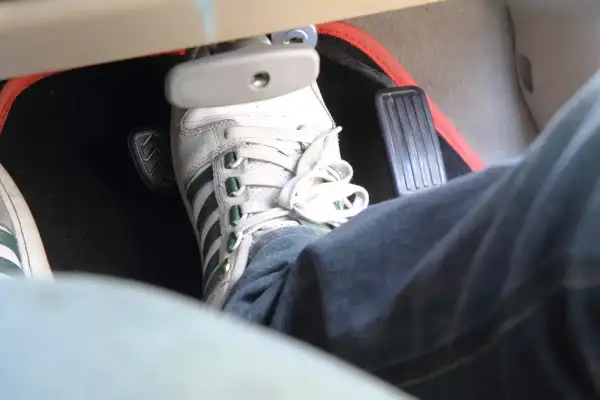 Pédale de frein enfoncée, signe d'un symptôme air dans circuit de freinage. La chaussure blanche à rayures vertes est sur la pédale.