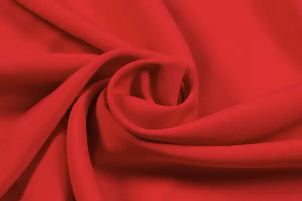 Roter Stoff, der sich zu einer Spirale drapiert. Die Textur ist glatt, was auf Lyocell oder Viskose hindeutet. Der Unterschied zwischen Lyocell und Viskose ist oft subtil.