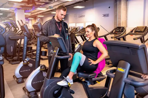 Trener pomaga kobiecie na rowerku stacjonarnym. Czy MCFit honoruje Multisport? Sprawdź, zanim zaczniesz trening!
