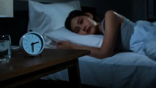 A woman lies awake in bed, staring at the clock. She's trying to figure out how to fall back asleep.