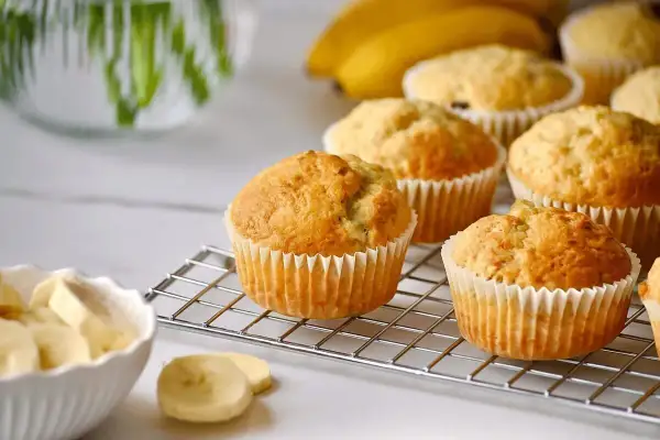 Frisch gebackene bananen muffins auf einem Gitter, daneben eine Schüssel mit Bananenscheiben.