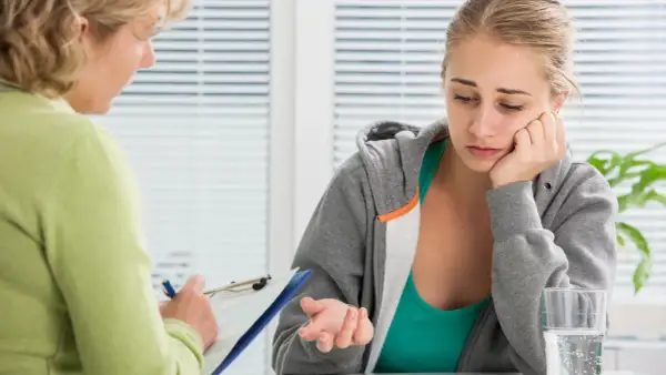 Una joven preocupada habla con un psicólogo que toma notas. La sesión se centra en cuanto cuesta un psicologo y cómo acceder a ayuda profesional.