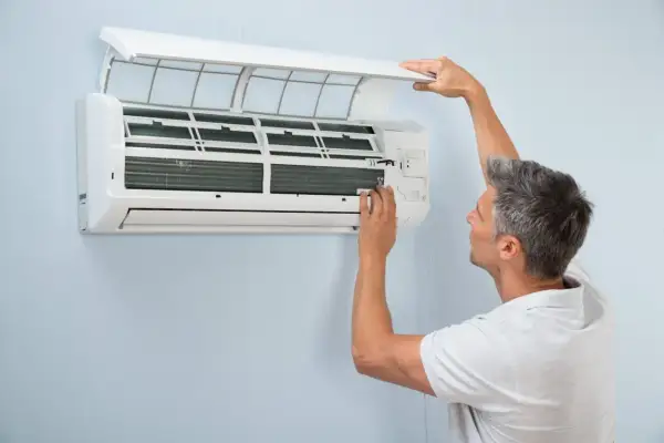 Mężczyzna sprawdza klimatyzację, która raz działa raz nie. Otwiera obudowę, by przyjrzeć się mechanizmowi.