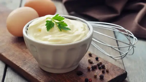 Cremige Mayonnaise ohne Ei, garniert mit Petersilie, neben Eiern und Pfefferkörnern.