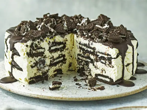 Cremige Oreo Torte mit Schokoladenguss und zerbröselten Keksen obendrauf. Ein Stück ist bereits angeschnitten.