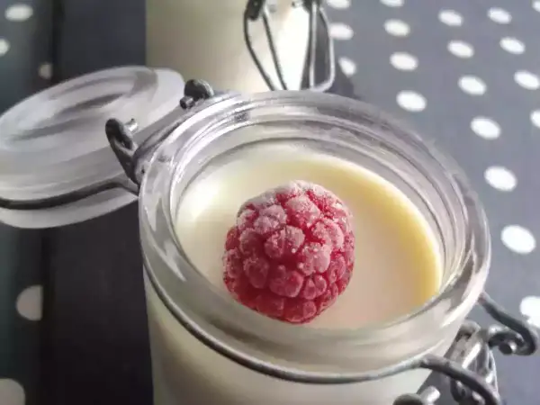 Délicieux panna cotta chocolat blanc, garni d'une framboise givrée, dans un pot en verre.