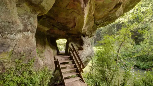 Holztreppe führt aus einer Felsgrotte auf dem schwarzachklamm wanderweg. Ein Fluss plätschert im Hintergrund.