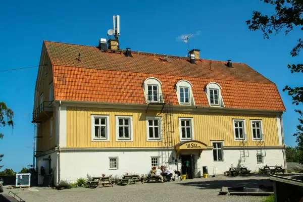Gult hus med orange tak, "Ut Sikten" skylt. Finnhamn vandrarhem, en plats för avkoppling och naturupplevelser.