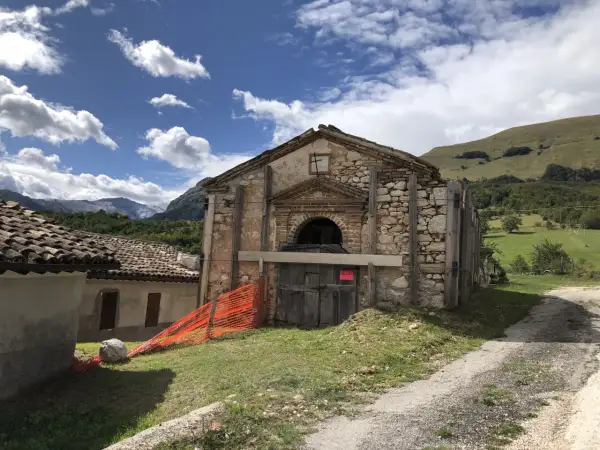 Il rifugio Città di Amandola, con la sua facciata in pietra e legno, è circondato da un paesaggio verdeggiante sotto un cielo azzurro con nuvole bianche.