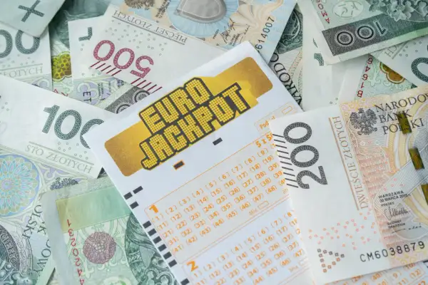 Kupon Eurojackpot na tle polskich banknotów. Czy to wyjaśnia, dlaczego lottomilionerzy z eurojackpot częściej uciekają z polski po wygranej?