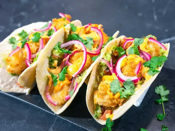 Fisktacos recept: Krispiga fiskbitar, krämig sås, rödlök och koriander i mjuka tortillabröd. En fest för smaklökarna!