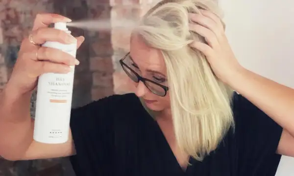 Kvinna med blont hår sliter torrschampo i håret för volym och textur.