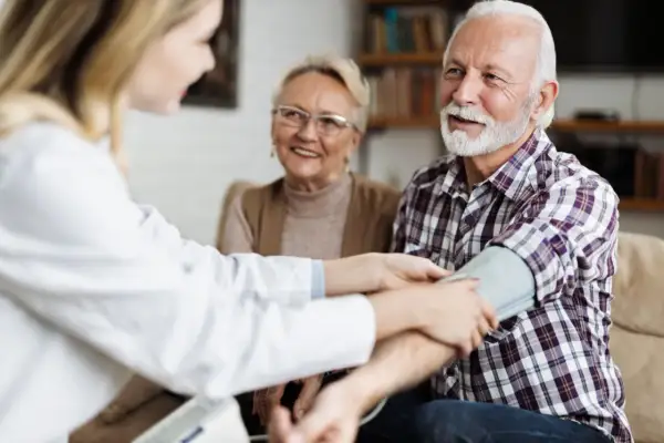 Un médecin vérifie la tension d'un homme âgé, 15/8 de tension, tandis que sa femme souriante observe.