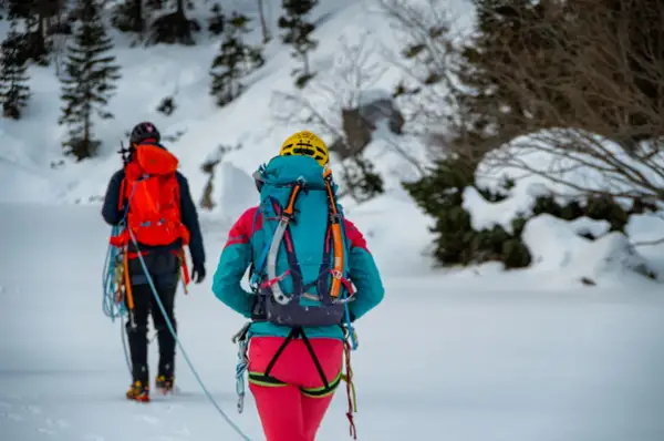 Dwóch alpinistów w zimowych strojach, z plecakami i sprzętem, przemierza ośnieżony teren. To inspiracja, co zabrać w góry zimą.