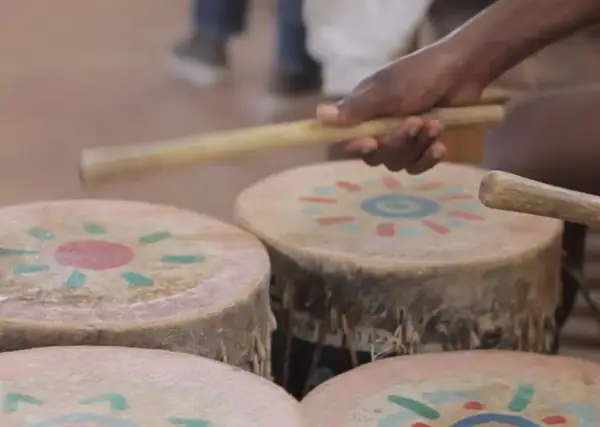 Mani che percuotono tamburi decorati con motivi solari, creando la vibrante musica africana.