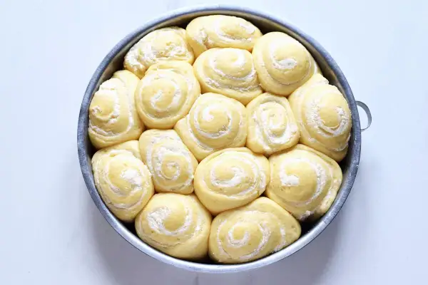 Torta di rose in teglia, soffici panini dolci con zucchero a velo, pronti per essere infornati.