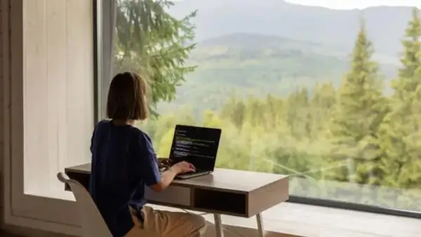 Persona trabajando en su portátil con vistas a un bosque y montañas. El estilo de vida de viajar trabajando es posible.