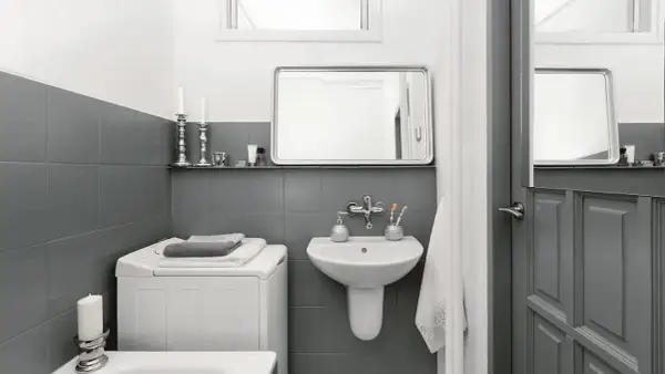 Baño moderno con azulejos grises, lavadora y lavabo. Un ejemplo de reformas de baños antes y después, con un estilo minimalista y funcional.