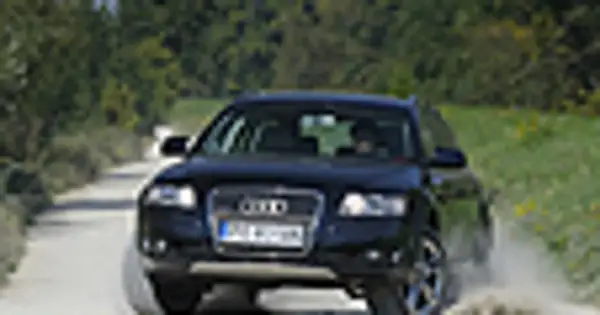Ciemny Audi allroad pokonuje piaszczystą drogę, wzbijając kurz.