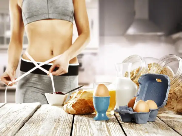 Kobieta mierzy talię, obok zdrowe śniadanie: jajka, płatki, mleko, sok. Idealny jadłospis na dieta 1 kg tygodniowo.