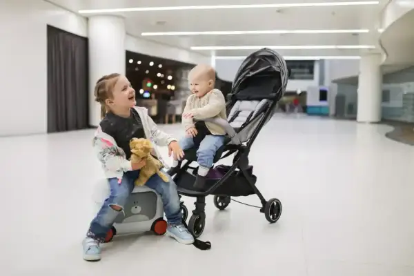 Dzieci w wózku dziecięcym Wizzair, starsza siostra trzyma misia, młodsza siedzi w wózku.