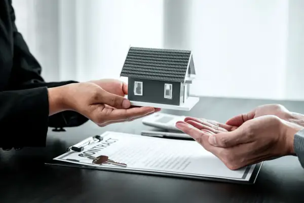 Manos entregan maqueta de casa sobre contrato. Posible exención IRPF venta vivienda heredada.