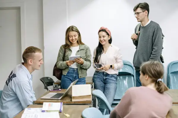 Grupa młodych ludzi dyskutuje o tym, ile trwa liceum dla dorosłych, przeglądając notatki i książki przy drewnianym stole.