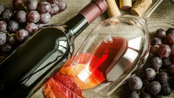 Uva Sangiovese, vitigno del Brunello di Montalcino, accompagna una bottiglia e un calice di vino rosso, su un tavolo di legno rustico.