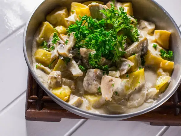 Pyszna potrawka z kurczaka ze śmietaną, grzybami i ziemniakami, udekorowana świeżą natką pietruszki.
