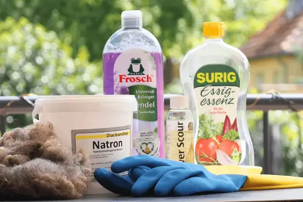 Wollprogramm Waschmaschine: Natron, Essigessenz und Reinigungsmittel für die schonende Wäsche. Blaue Handschuhe liegen bereit.