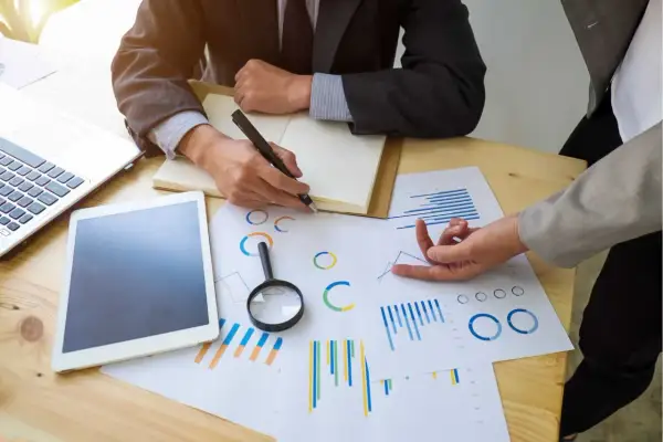 Deux personnes analysent des graphiques et des données pour un audit énergétique. Un ordinateur portable et une tablette sont sur la table.