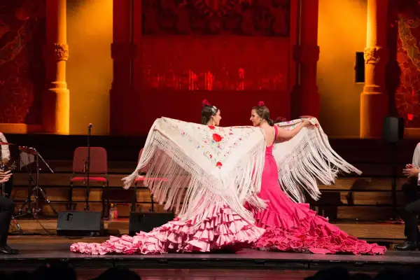 Dos bailarinas de flamenco, con vestidos rosas y mantones bordados, despliegan su arte. El escenario tiene un aire de tener aje.