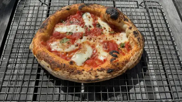 En perfekt napolitansk pizza med bubblig, bränd kant, tomatsås och smält mozzarella på ett galler.