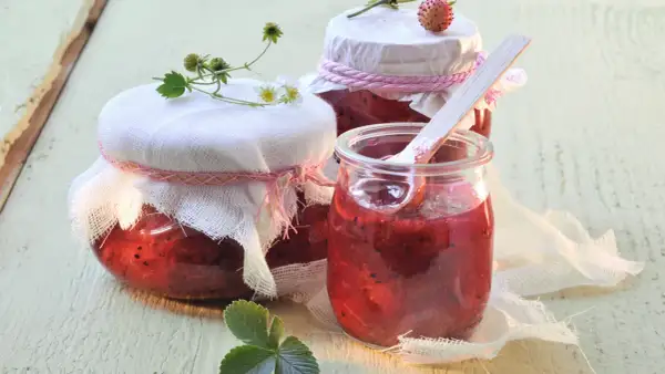 Gläser mit selbstgemachtem Erdbeerkompott, bereit zum Einkochen. Ein Holzlöffel steckt in einem Glas.