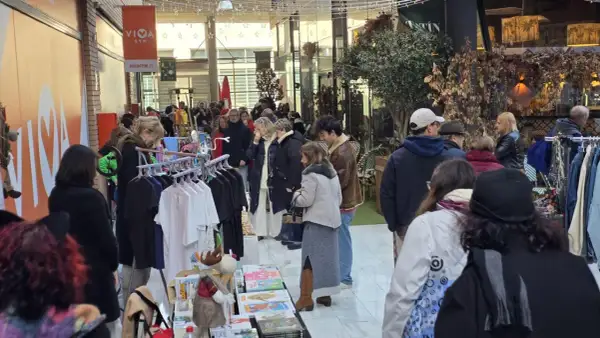Gente comprando en un rastro de Zaragoza. Hay ropa colgada en percheros y puestos con libros y adornos.