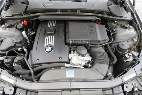 Silnik BMW 325i. Widok na pokrywę silnika z logo BMW, elementy układu dolotowego i chłodzenia.