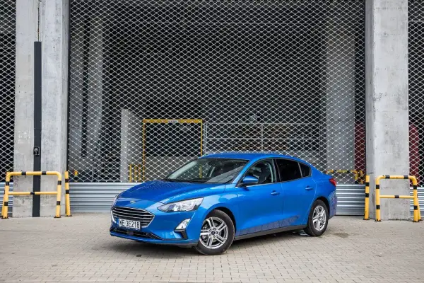 Niebieski Ford Focus 1.0 EcoBoost stoi przed metalową bramą.