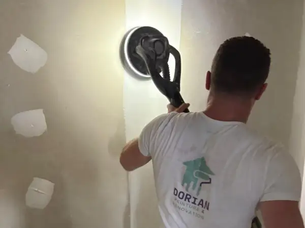 Un artisan utilise une ponceuse girafe pour lisser un mur en placo. C'est la ponceuse idéale pour un travail de finition impeccable.