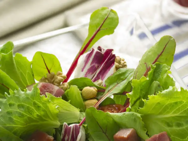 Ensalada fresca con brotes tiernos, nueces y trozos de jamón.