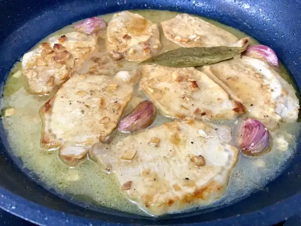 Filetes de lomo al ajillo dorándose en una sartén con ajo y laurel.