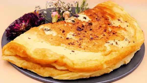 Puszysty omlet dla niemowlaka, delikatnie przyrumieniony, z ozdobnymi suszonymi kwiatami na talerzu.