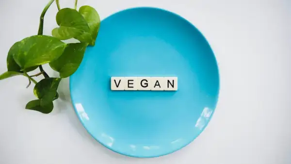 Niebieski talerz z literami "VEGAN" i zielonymi liśćmi. To symbol tego, co to jest weganizm: dieta bez produktów odzwierzęcych.