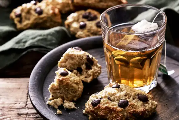 Choklad scones på ett fat med en kopp te. En härlig fika, men tänk på scones kalorier om du vill hålla koll.