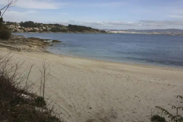 Arena dorada en la playa temperans, con el mar azul y una ciudad al fondo.
