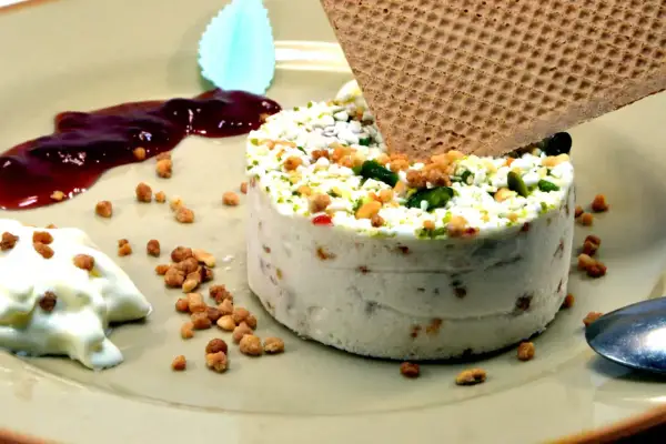 Un délicieux nougat glacé, parsemé de fruits secs et de pistaches, servi avec un coulis de fruits rouges et une touche de crème.